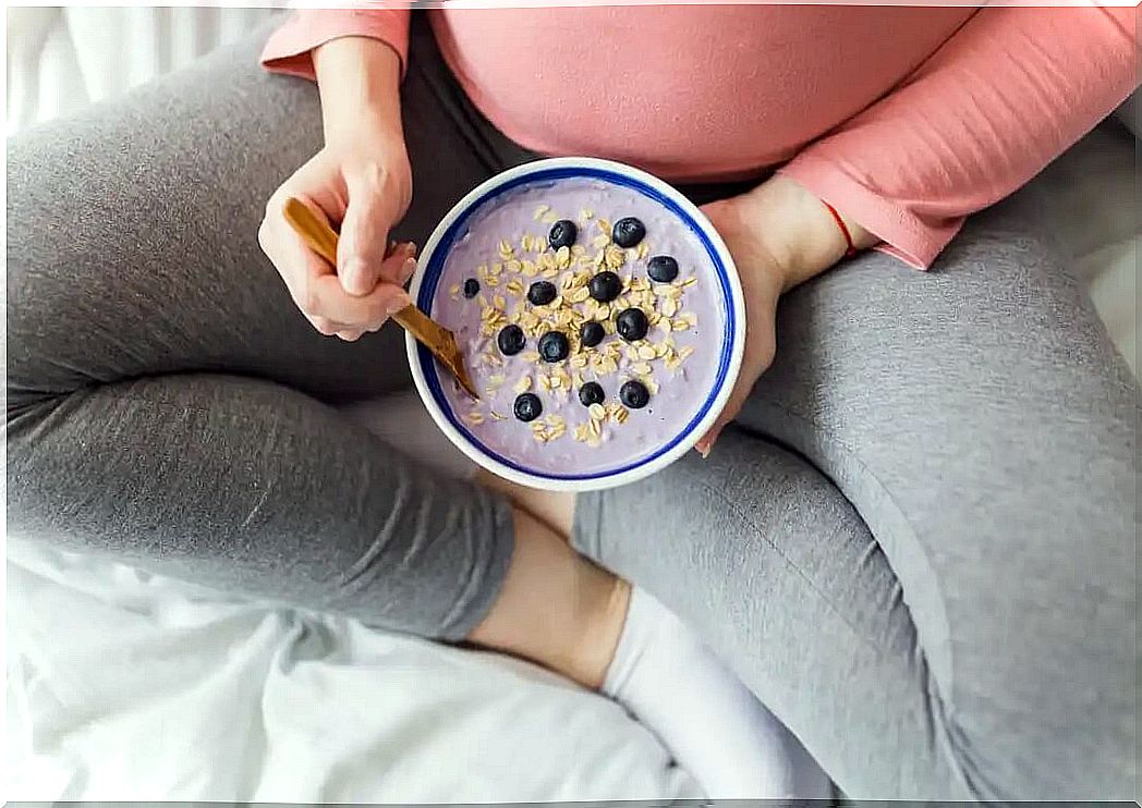 Mulher grávida comendo iogurte com cereais e frutas.